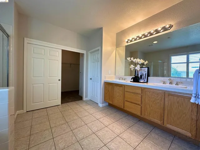 Full bathroom with double vanity, a stall shower, light tile patterned floors, a spacious closet, and a textured ceiling