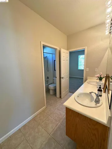 Full bathroom featuring double vanity, light tile patterned flooring, a textured ceiling, and a textured wall