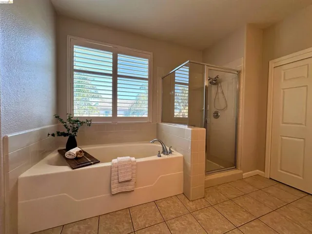 Full bathroom featuring a bath, a stall shower, light tile patterned floors, and a textured wall