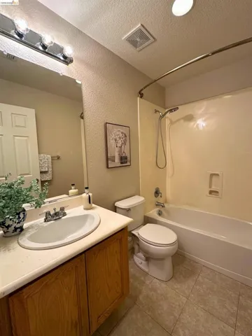 Bathroom featuring vanity, a textured ceiling,  shower combination, a textured wall, and light tile patterned floors