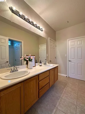 Full bathroom with double vanity, light tile patterned flooring, and a textured ceiling