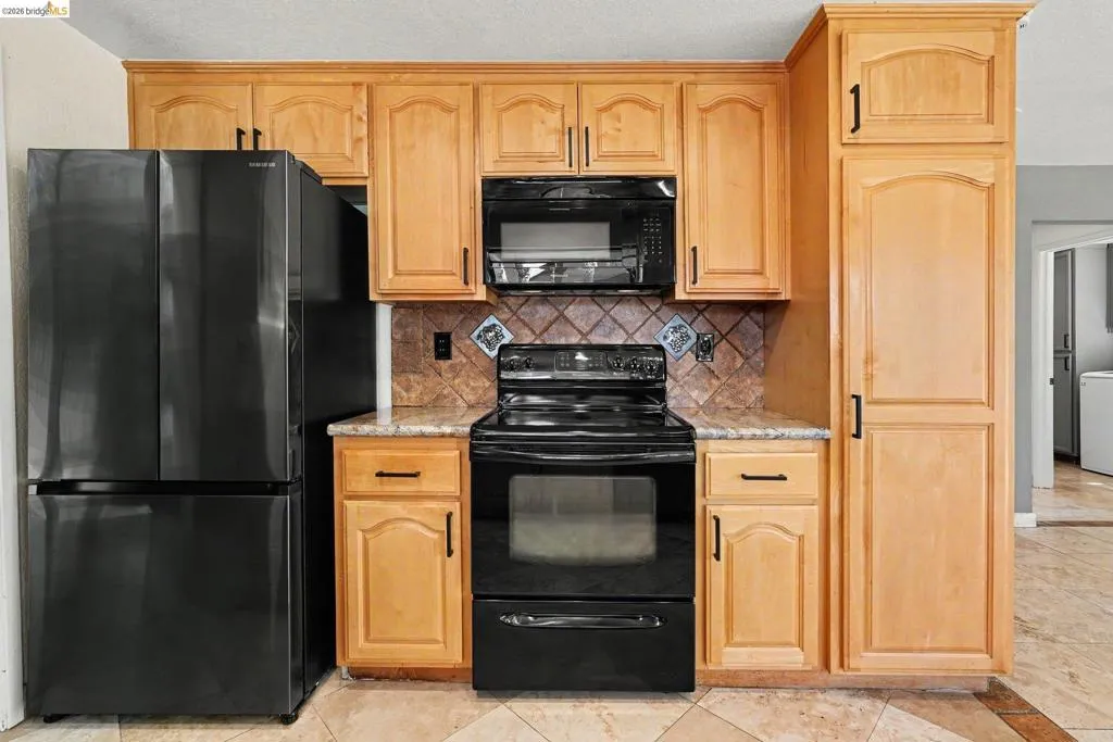 Kitchen featuring light wood cabinetry with dark hardware, black appliances, a tile backsplash, and light-colored countertops
