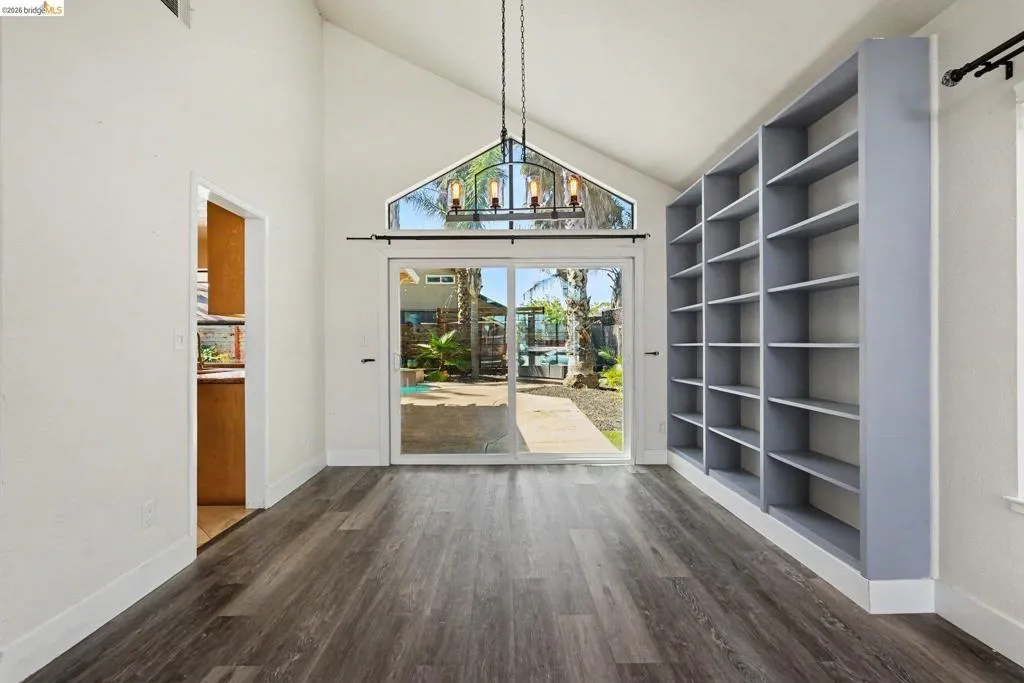 Vaulted ceiling room featuring wood-finish flooring, a built-in shelving unit, and a sliding glass door with an overhead transom window