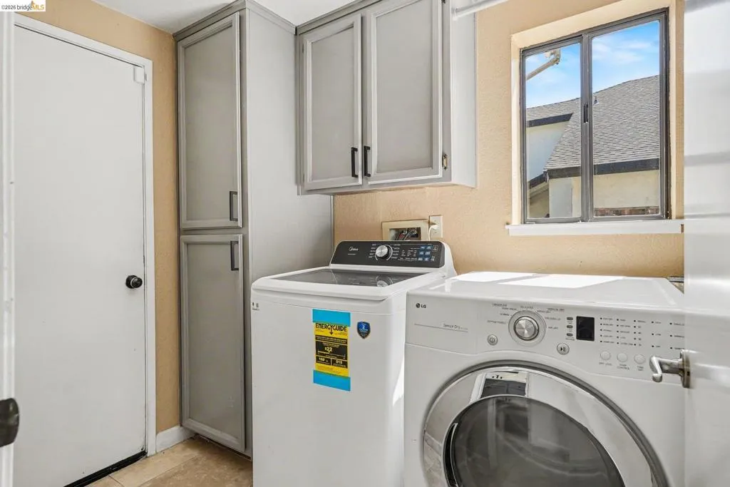 Laundry area featuring tile flooring, built-in grey cabinetry with black hardware, and a window