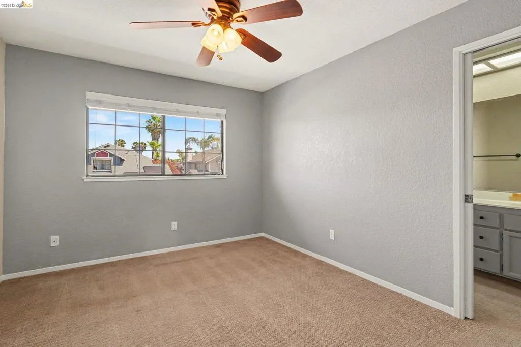 Carpeted room with a ceiling fan featuring a window with horizontal blinds and an adjacent bathroom entry