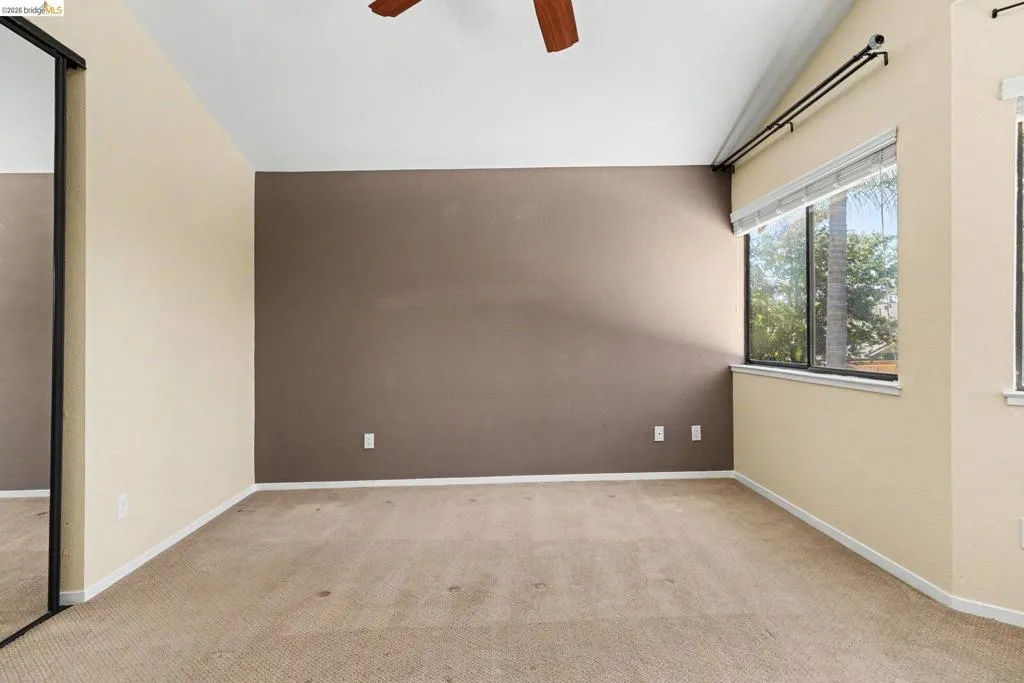 Carpeted room featuring a vaulted ceiling and a wood-finish ceiling fan