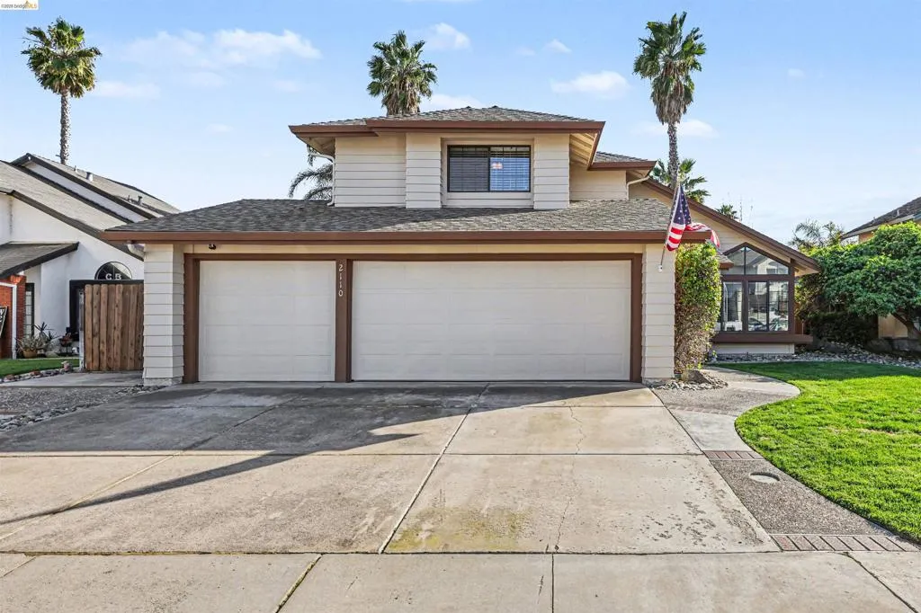 View of front of property with concrete driveway, a front yard, roof with shingles, a sunroom, and an attached garage