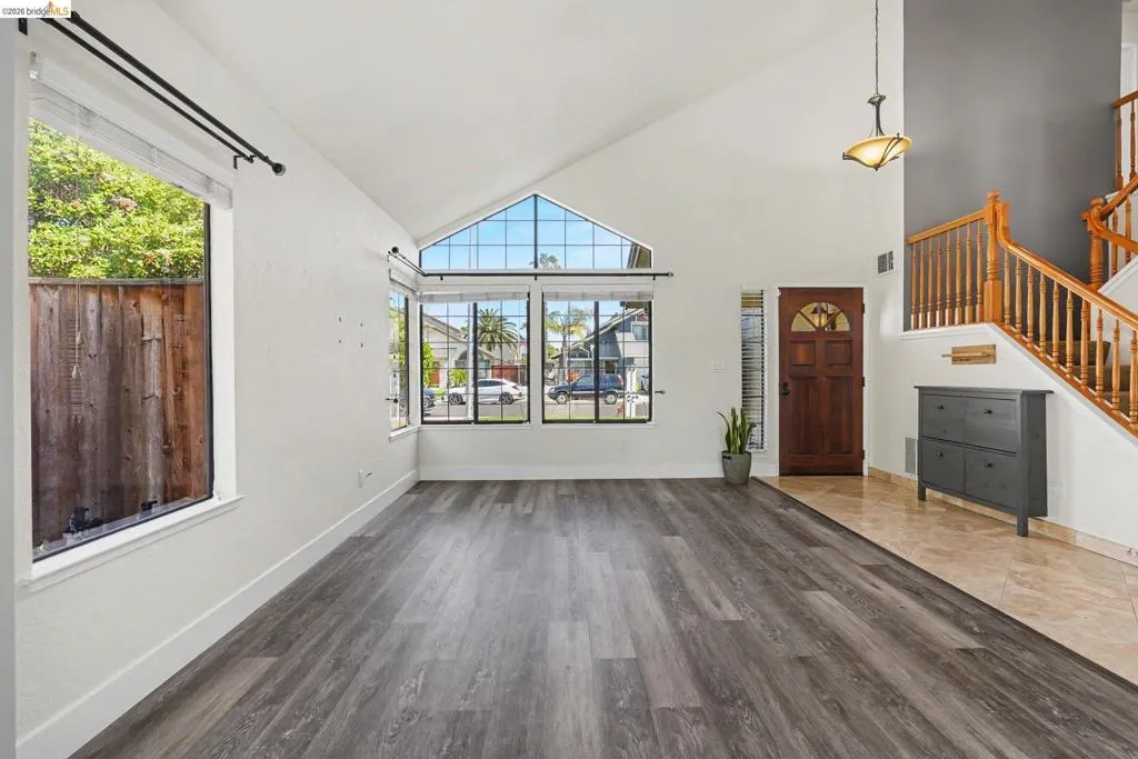 Vaulted ceilings featuring a large triangular window, wood-finish flooring, a wood front door with an arched glass insert, a tiled entryway, and a wooden staircase with balusters