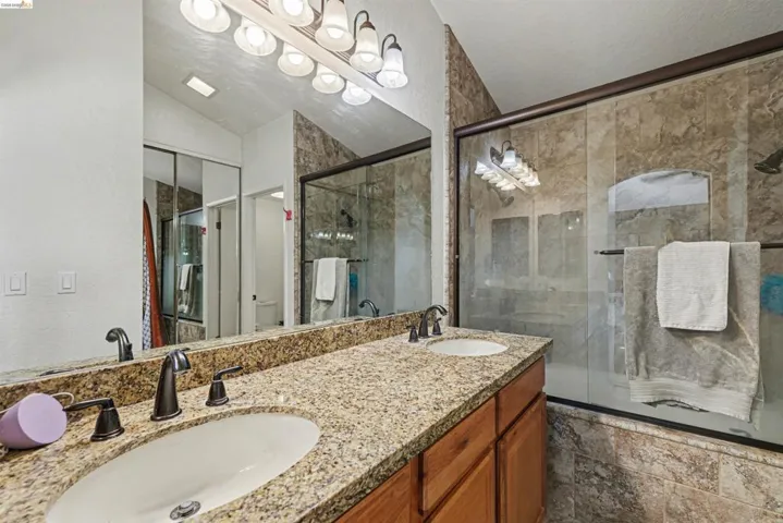 Bathroom featuring double vanity, lofted ceiling, tiled shower / bath combo, and a textured wall