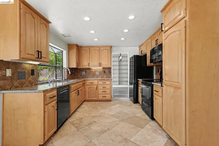 Kitchen featuring light wood cabinetry, a tiled backsplash, and stone countertops