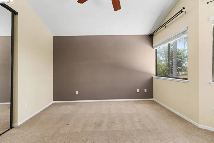 Carpeted room featuring a vaulted ceiling and a wood-finish ceiling fan
