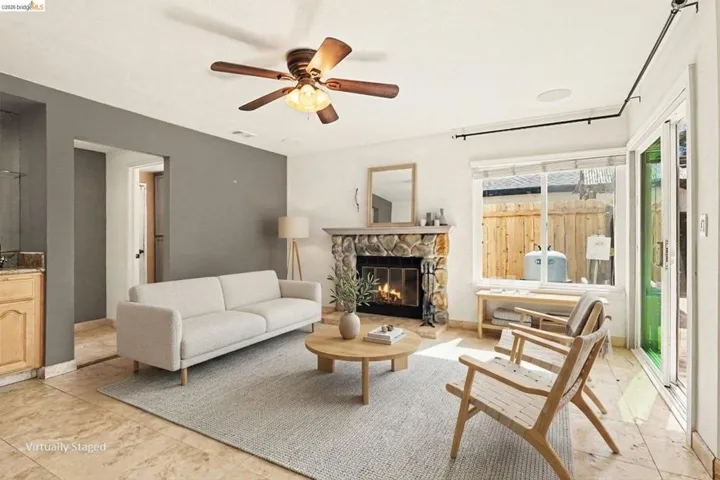 Living area featuring a stone fireplace, wood-finish ceiling fan, and tile flooring