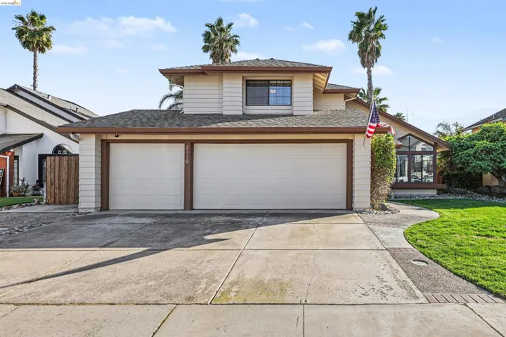 View of front of property with concrete driveway, a front yard, roof with shingles, a sunroom, and an attached garage