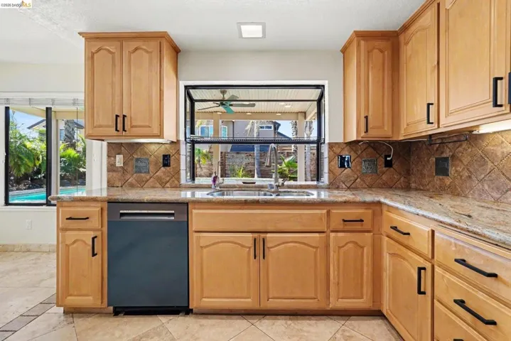 Kitchen featuring wood cabinetry with black hardware, granite countertops, and a tiled backsplash