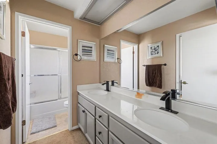 Bathroom with double vanity, shower / bath combination with glass door, and a textured wall