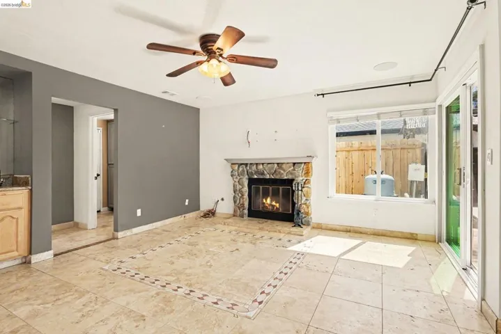 Spacious living area featuring a stone-clad fireplace, tile flooring with decorative inlay, and a ceiling fan