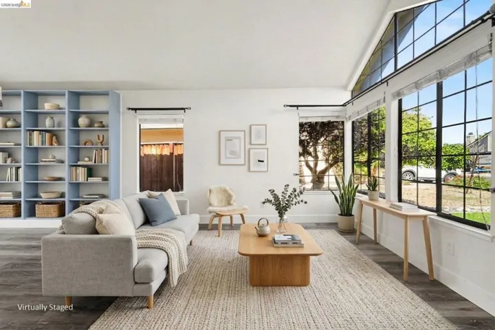 Living area featuring vaulted ceilings, a full wall of built-in shelving, expansive picture windows with black framing, wood-finish flooring, and white walls