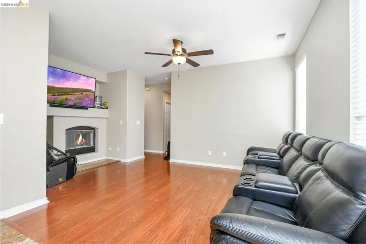 living area featuring light wood-type flooring, a ceiling fan, and a glass covered fireplace