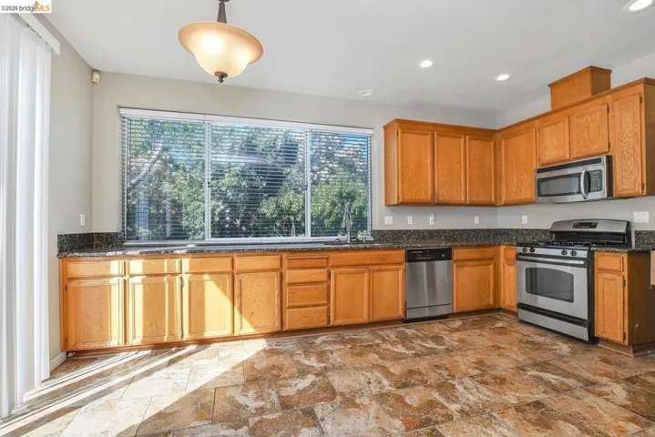 kitchen featuring stainless steel appliances, dark stone finish floors, decorative light fixtures, and plenty of natural light
