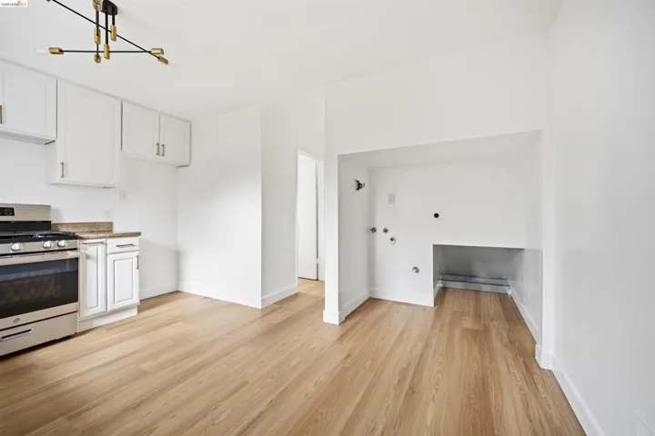 Kitchen with white cabinets, stainless steel range with gas cooktop, light stone countertops, and light wood-type flooring