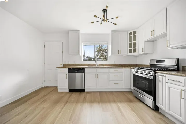 Kitchen featuring stainless steel appliances, white cabinets, glass insert cabinets, light wood finished floors, and dark stone counters