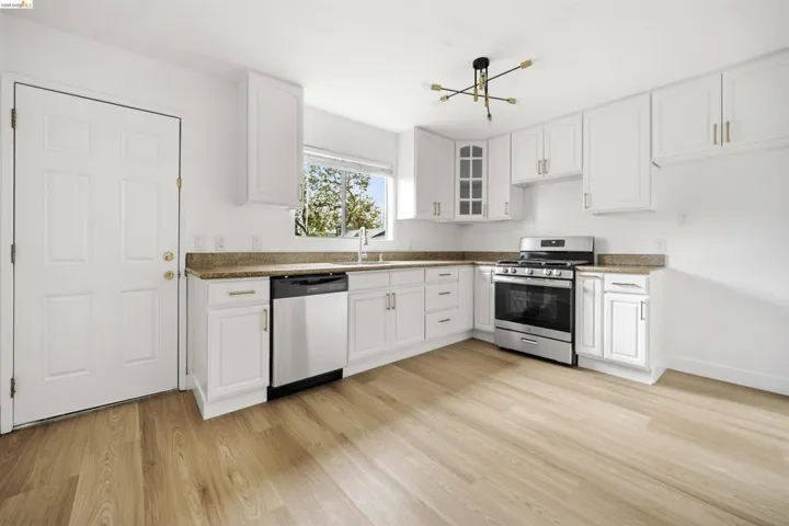 Kitchen with stainless steel appliances, white cabinets, glass fronted cabinets, light wood finished floors, and dark stone countertops