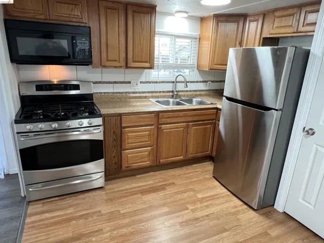 Kitchen featuring stainless steel appliances, light wood-type flooring, wood finish cabinets, and light countertops