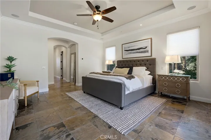 Expansive primary bedroom featuring a tray ceiling, abundant natural light, and peaceful views of the lush backyard landscape.
