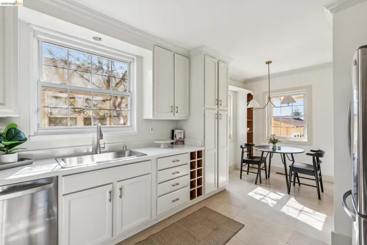 Kitchen featuring stainless steel appliances, light countertops, ornamental molding, white cabinetry, and hanging light fixtures