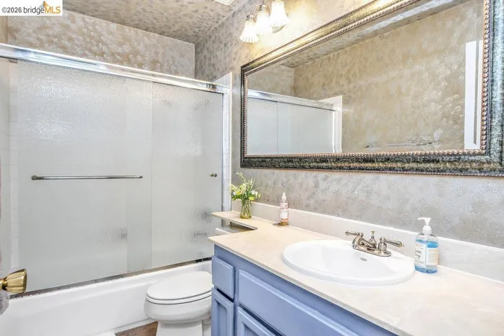 Bathroom featuring vanity, combined bath / shower with glass door, and wallpapered walls