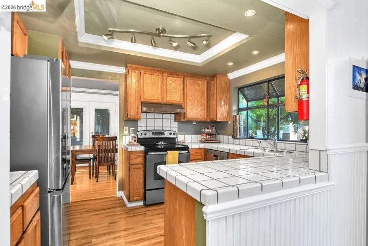 Kitchen featuring wood finish cabinetry, tile countertops, stainless steel appliances, a peninsula, and crown molding