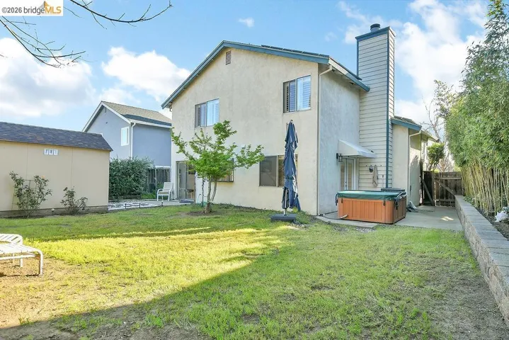 Back of property with a hot tub, a patio area, stucco siding, and a chimney