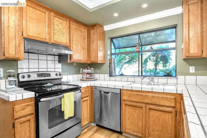 Kitchen with tile counters, stainless steel appliances, backsplash, ornamental molding, and wood finish cabinets