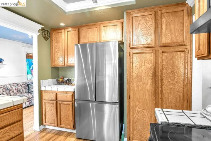 Kitchen with freestanding refrigerator, ornamental molding, light wood finished floors, tile counters, and wood finish cabinets