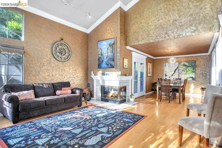 Living area featuring ornamental molding, lofted ceiling, a tile fireplace, light wood finished floors, and track lighting