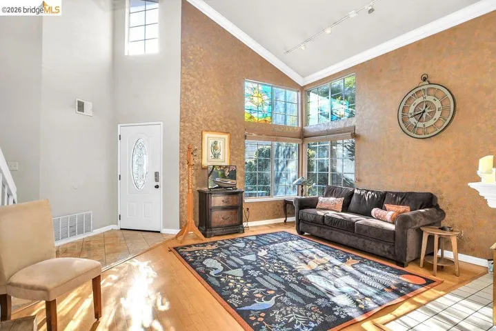 Living room with plenty of natural light, vaulted ceiling, rail lighting, ornamental molding, and light wood finished floors