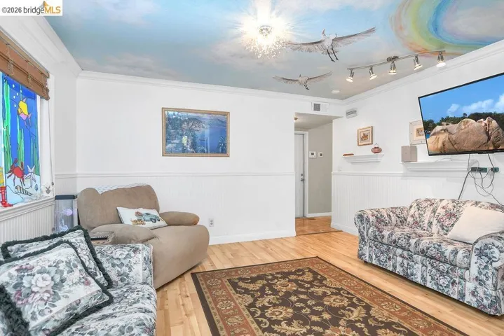 Living room with crown molding, light wood finished floors, and wainscoting