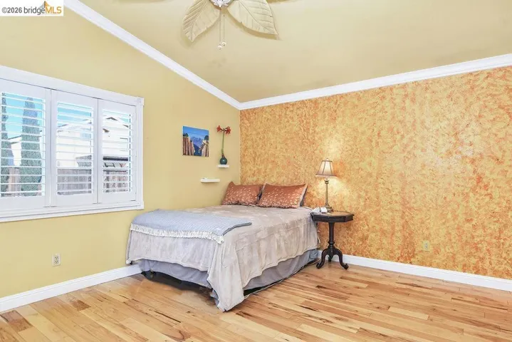 Bedroom with light wood-style floors, ornamental molding, wallpapered walls, and ceiling fan