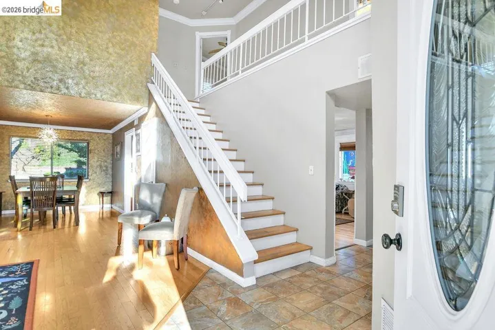 Foyer entrance with ornamental molding, plenty of natural light, a high ceiling, suspended lighting, and light wood finished floors