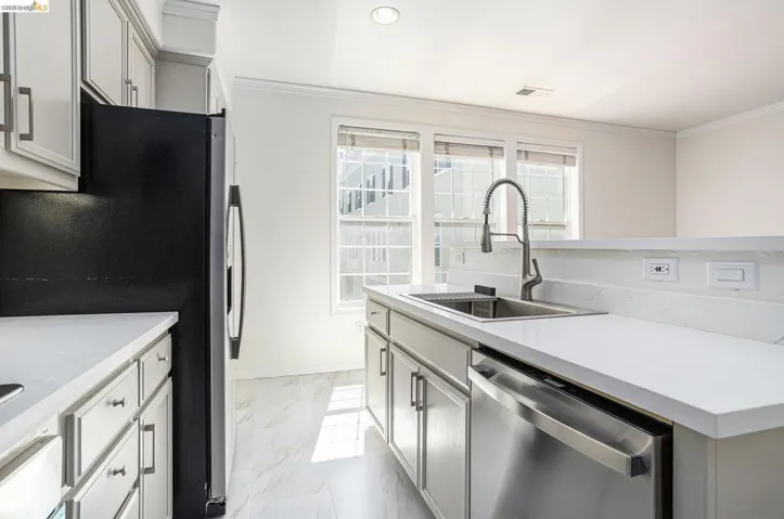 Kitchen featuring stainless steel appliances, light stone counters, ornamental molding, light marble finish floors, and gray cabinets