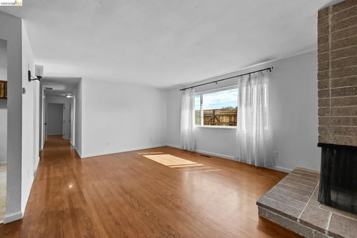 Unfurnished living room featuring a brick fireplace, wood finished floors, and a textured ceiling