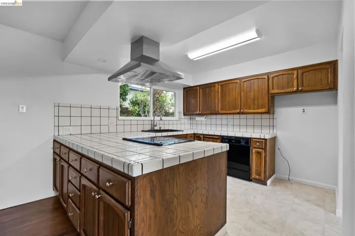 Kitchen featuring tile counters, backsplash, black appliances, and a peninsula