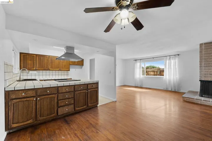 Kitchen featuring tile countertops, dark wood-type flooring, decorative backsplash, extractor fan, and a ceiling fan
