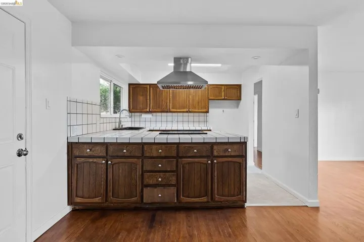 Kitchen with tile counters, range hood, dark wood-type flooring, backsplash, and recessed lighting