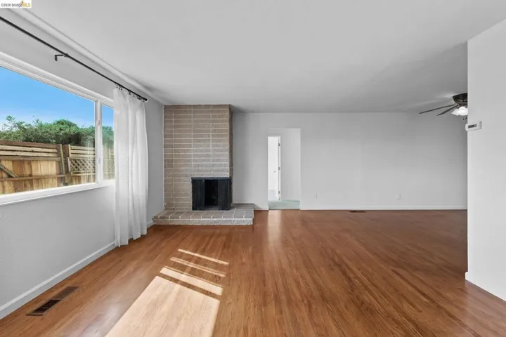 Unfurnished living room with ceiling fan, light wood-style floors, and a brick fireplace
