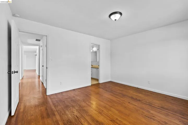 Unfurnished bedroom featuring dark wood-style flooring and ensuite bath