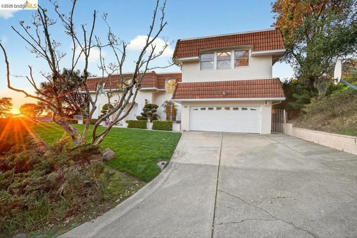 View of front of home with a tiled roof, an attached garage, driveway, a front lawn, and stucco siding