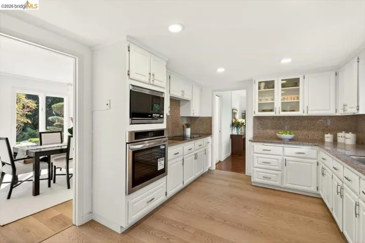 Kitchen featuring white cabinets, stainless steel appliances, dark stone countertops, glass insert cabinets, and recessed lighting