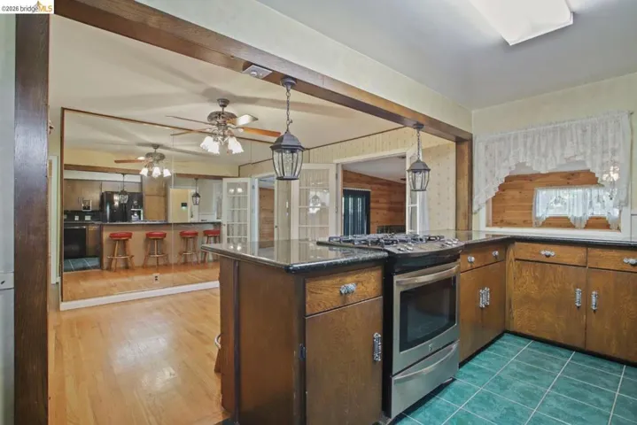Kitchen featuring stainless steel range with gas cooktop, black fridge, beam ceiling, hanging light fixtures, and a ceiling fan