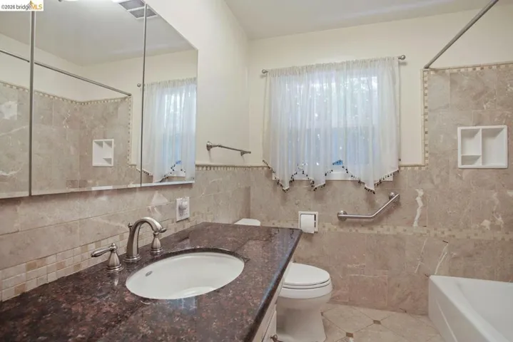 Full bath featuring vanity, light tile patterned floors, tile walls, plenty of natural light, and shower / tub combination